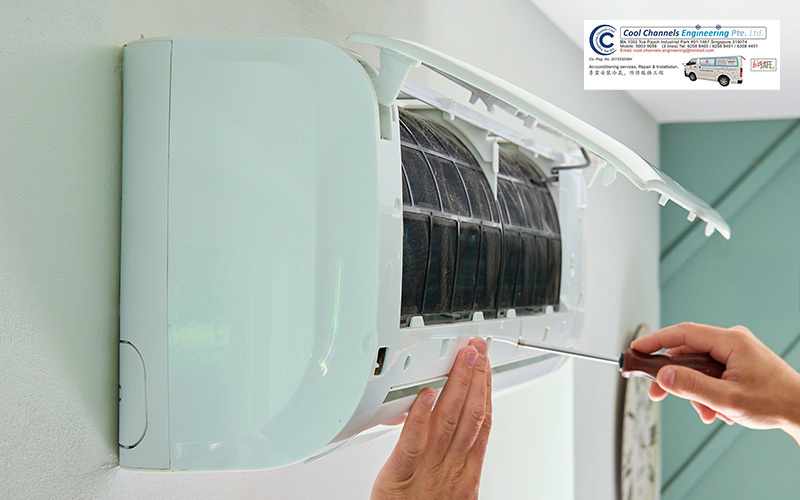 Person using screwdriver to service wall-mounted air conditioner with front panel open, revealing internal components.