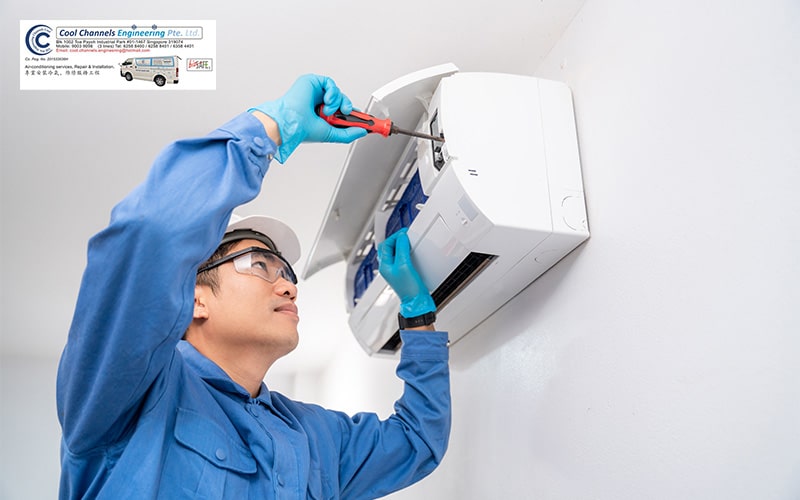 Technician in blue uniform using a screwdriver to service a wall-mounted aircon unit.